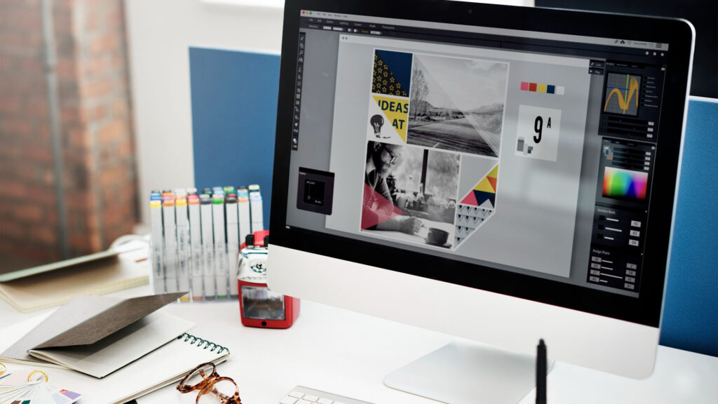 Auf einem Desktop-Computer wird ein Grafikdesignprojekt mit einem geöffneten Website-Navigationsfeld angezeigt. In der Nähe liegen ein Skizzenbuch, eine Brille und verschiedene Büromaterialien auf dem Schreibtisch.